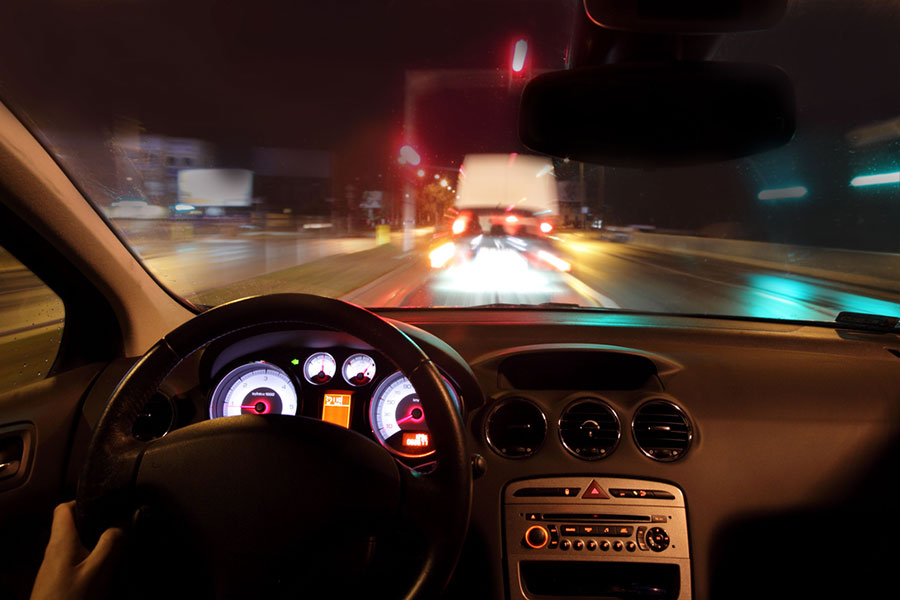 Image from the driver's perspective on a dark multi-lane highway with dashboard and blurry lights.