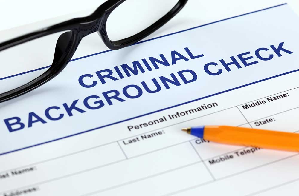 Close-up of a background check form labeled 'Criminal Background Check' with black glasses resting on top and an orange pen nearby.